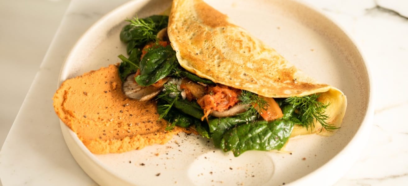 An image of a folder omelette on a white, high-lipped plate with a filling of green vegetables.